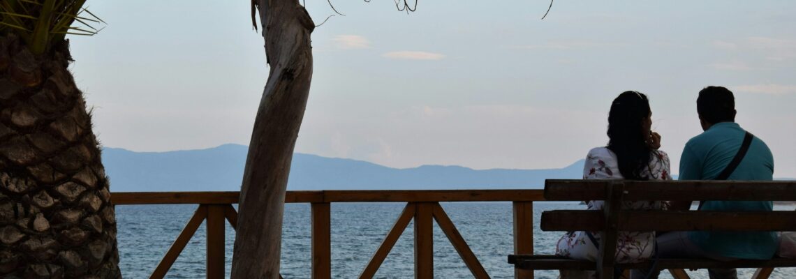 Couple sitting on a bench looking toward the ocean.