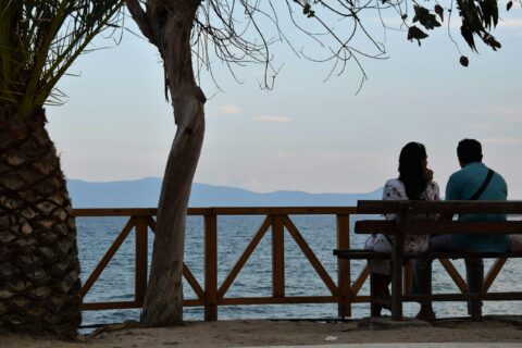 Couple sitting on a bench looking toward the ocean.