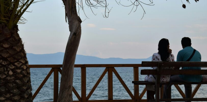 Couple sitting on a bench looking toward the ocean.