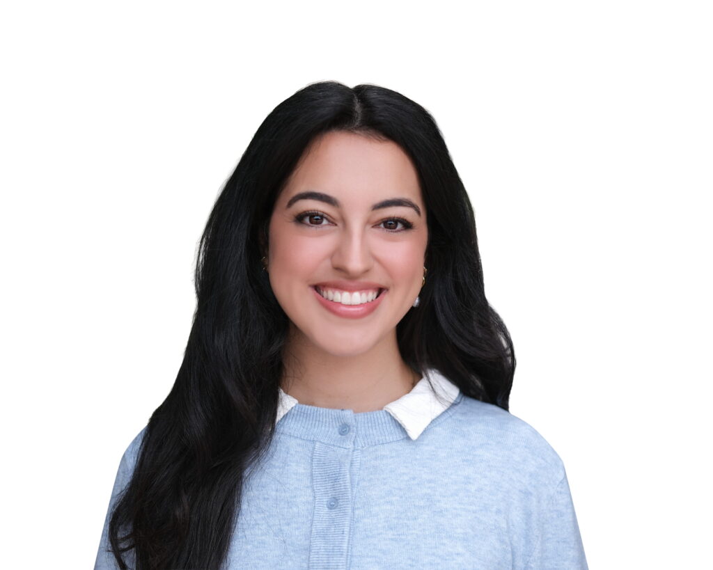 Smiling woman with long dark hair wearing a light blue sweater and white collar, against a white background.