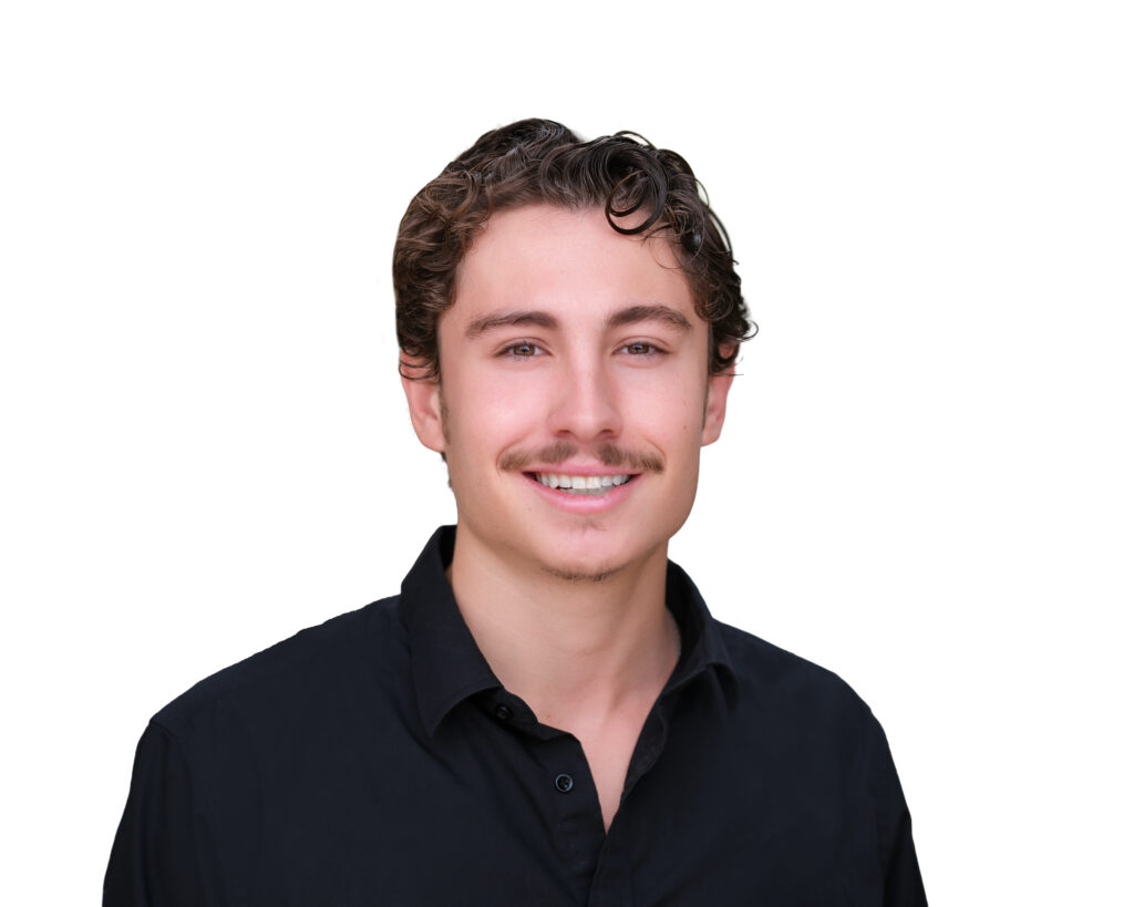Head-and-shoulders portrait of a young man with dark wavy hair, wearing a black button-up shirt, smiling against a white background.